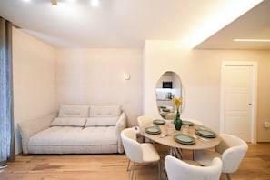 A modern living room with a sofa, a dining table set for four, and a large mirror. - Vimini Horizon (Bari)