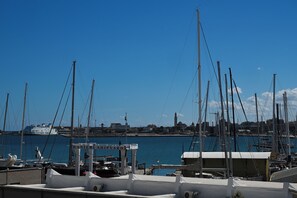 A marina with multiple sailboats docked, a clear blue sky, and a distant cityscape. - Vimini Horizon (Bari)