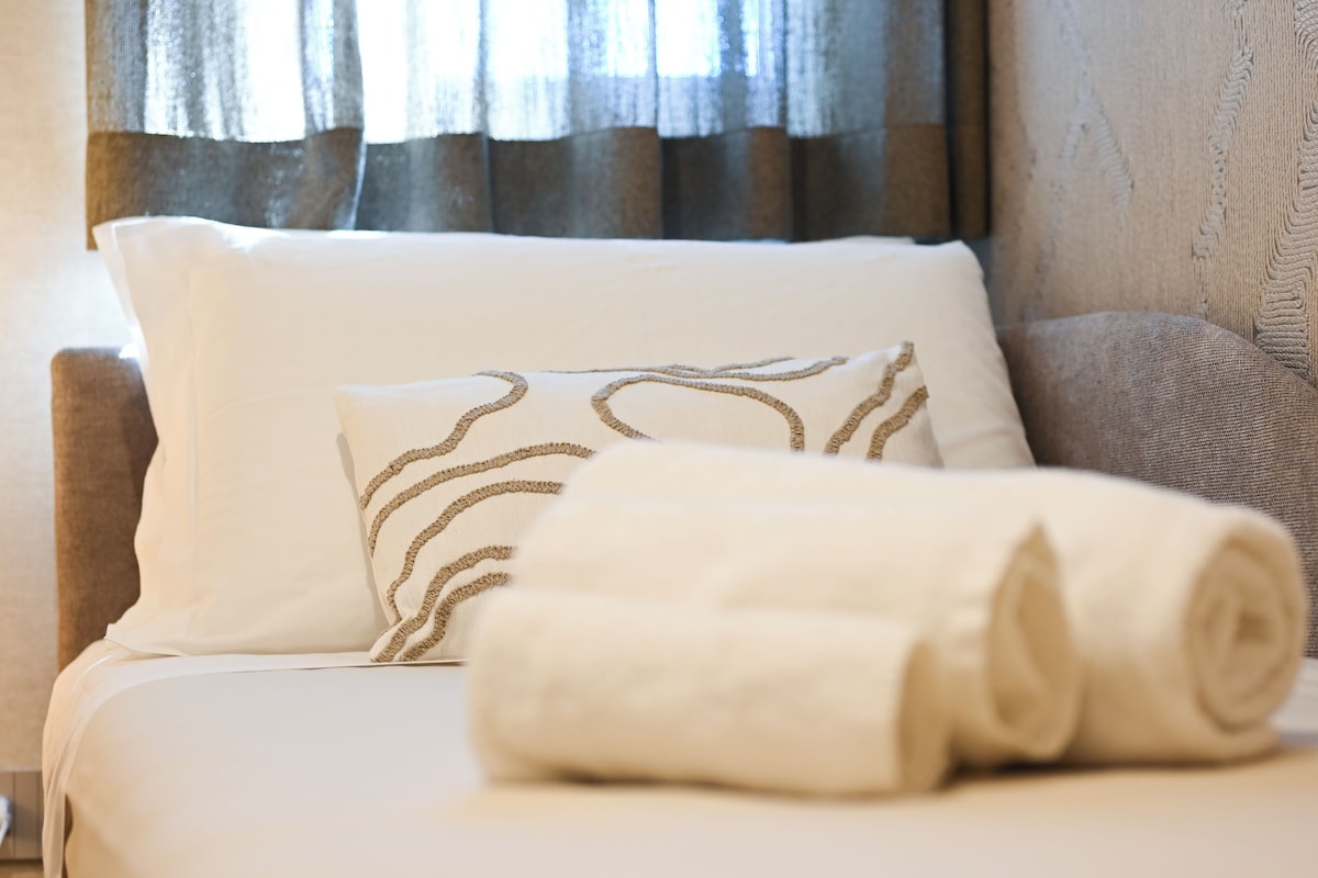 A neatly made bed with a rolled white towel and a pillow with a woven pattern.