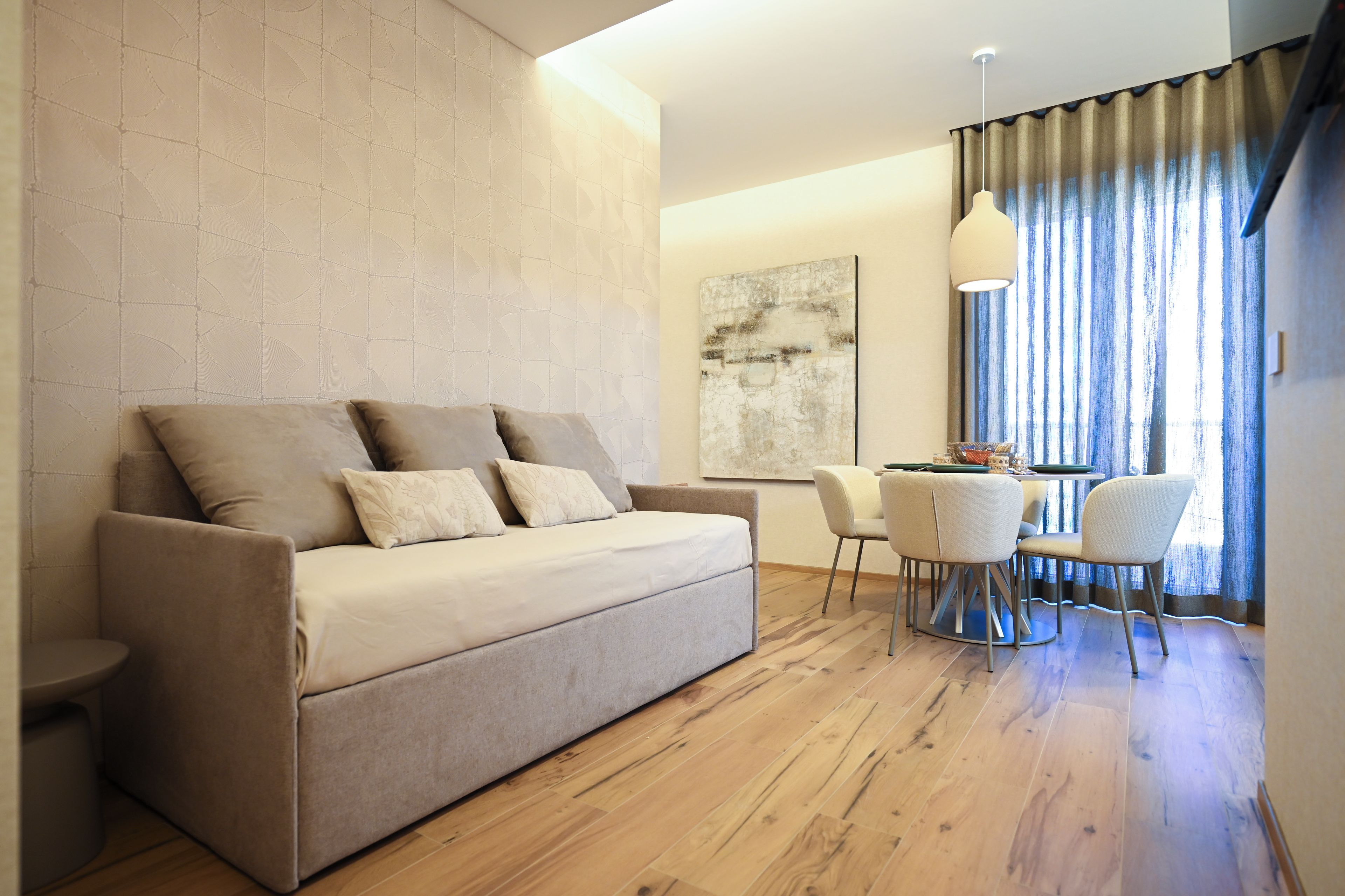 Ein modernes Wohnzimmer mit einer Couch, einem Esstisch mit Stühlen und einem großen Fenster mit Vorhängen.