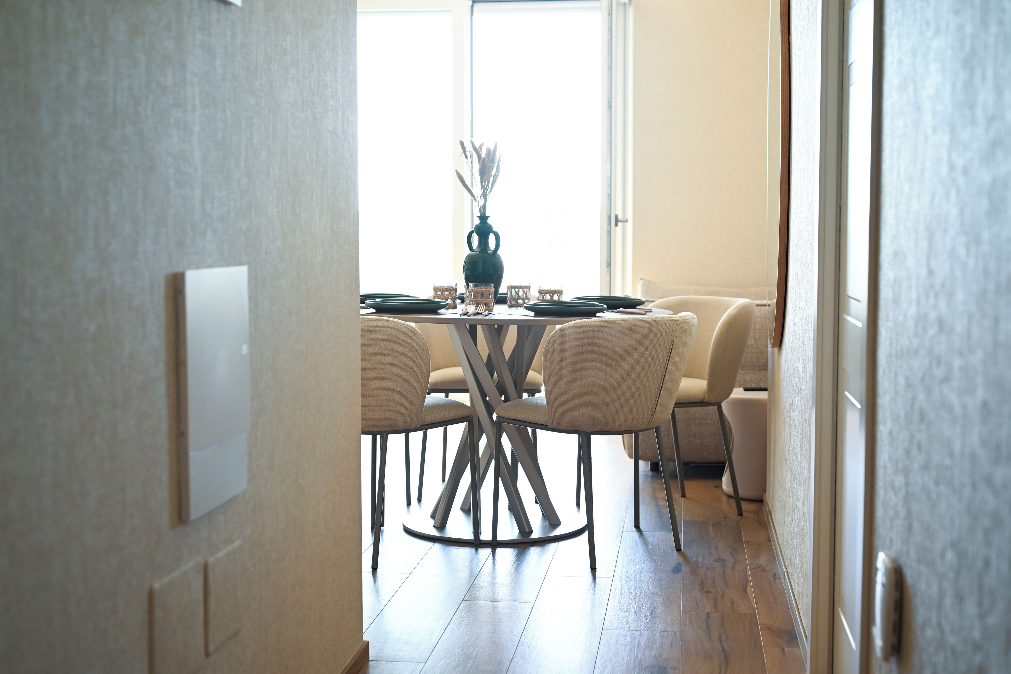 An interior view of a dining area with a round table, chairs, and a vase with dried plants.