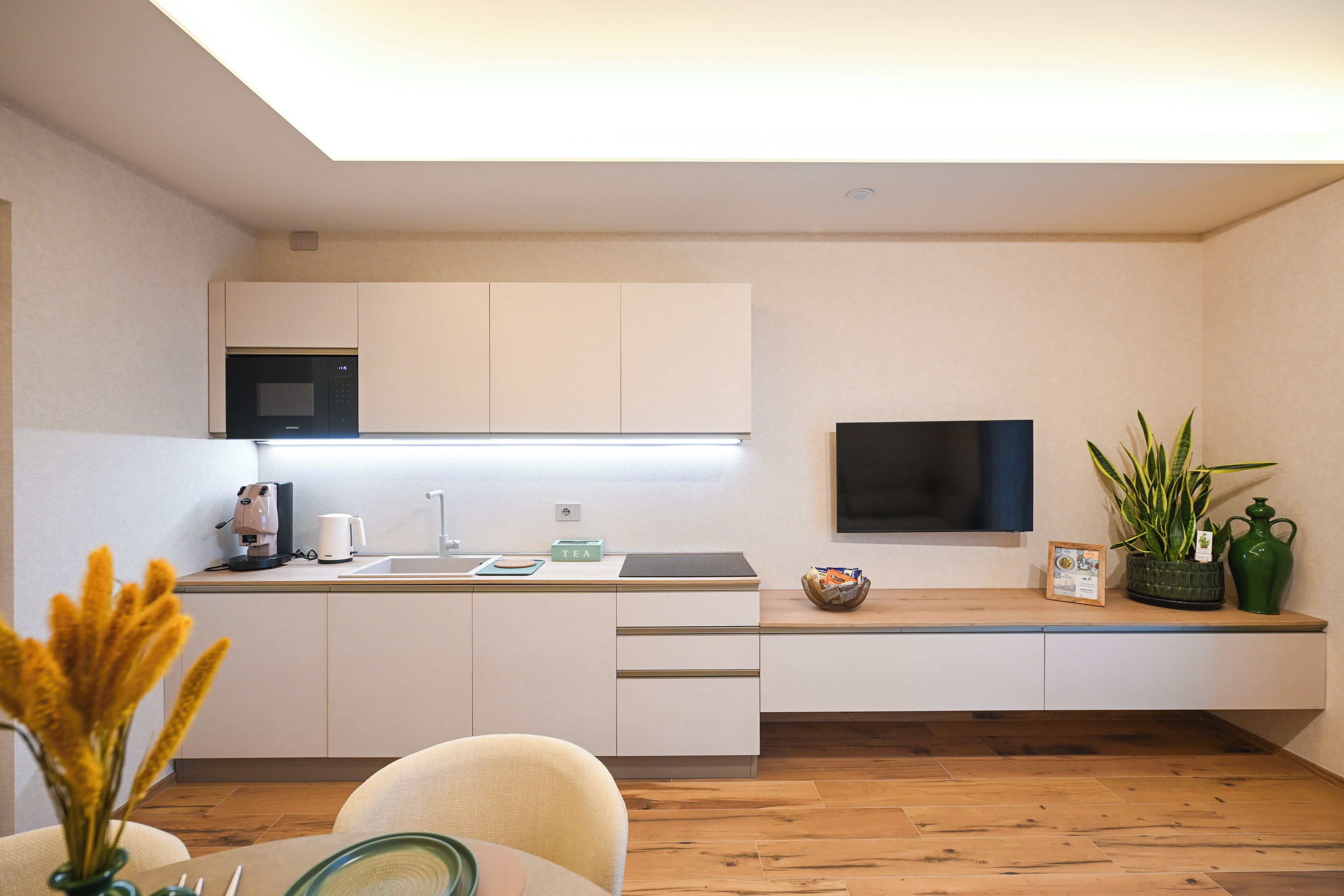 A modern kitchen with white cabinetry, a built-in microwave, and a flat-screen TV.
