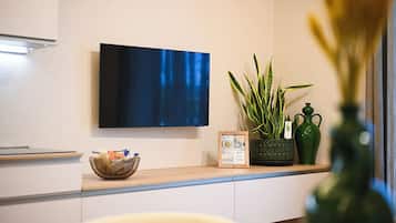 A modern kitchen with a flat-screen TV mounted on the wall, a bowl of snacks on the counter, and a potted plant.