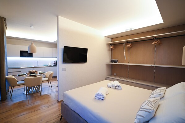 A modern hotel room with a bed, a TV, a kitchenette, and a dining area. - Vimini Horizon (Bari)