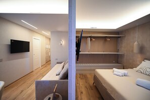 A modern hotel room with a flat-screen TV, a bed with white linens, a seating area with cushions, and a wardrobe with hanging clothes. - Vimini Horizon (Bari)