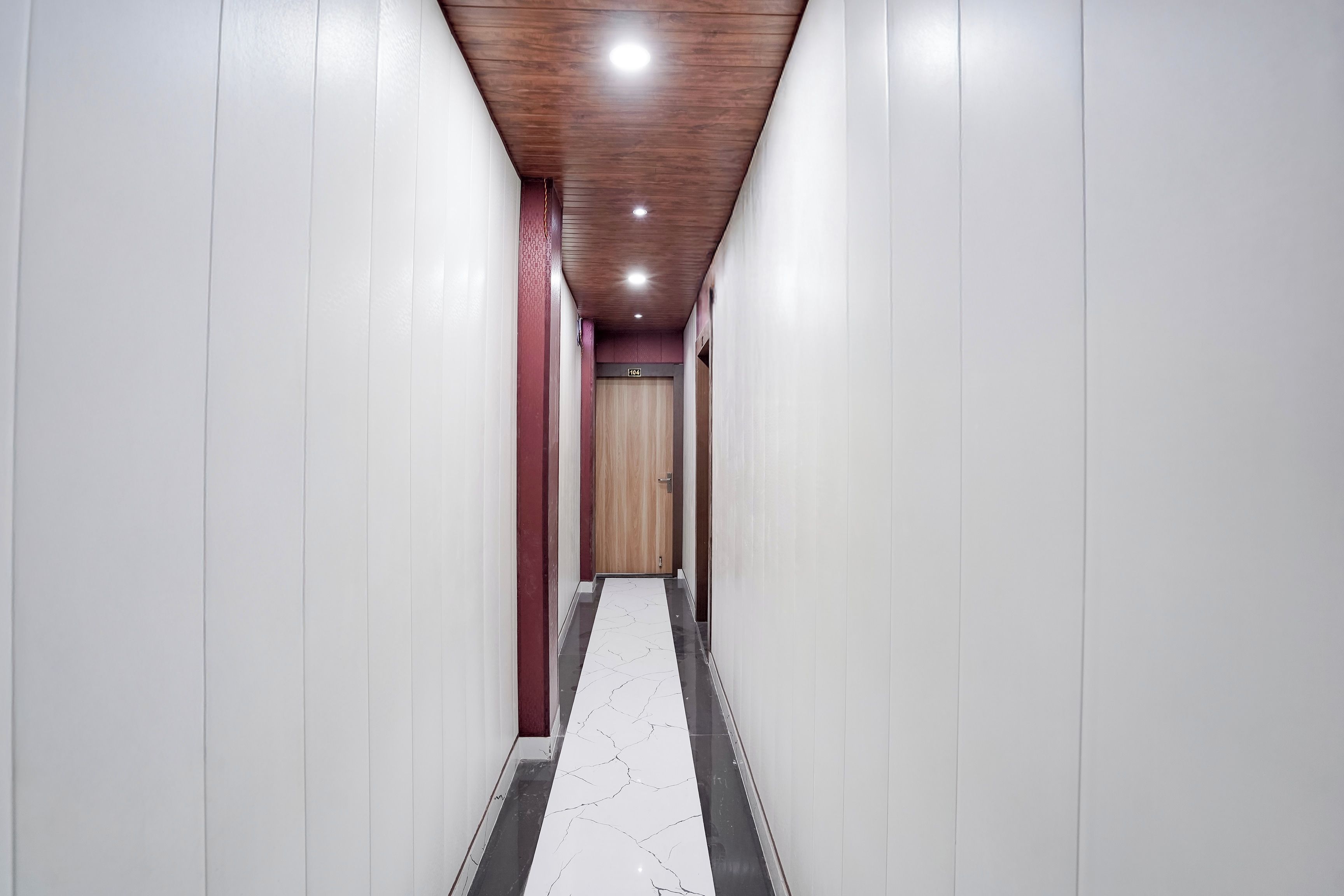 Un couloir aux murs blancs, doté d’un sol en marbre et d’un plafond en bois.