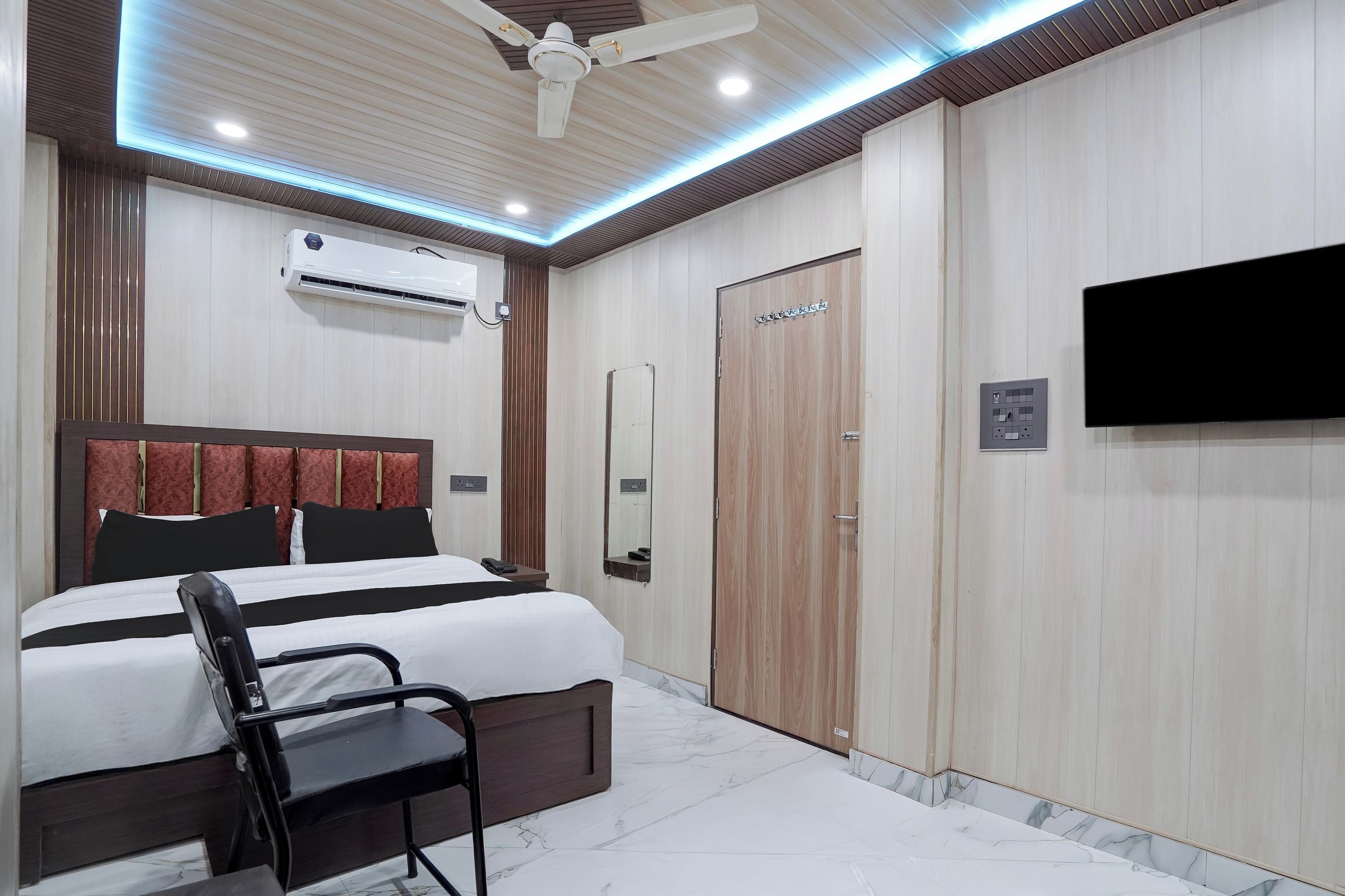 Una habitación de hotel con cama, sillón, televisor, equipo de aire acondicionado y armario.