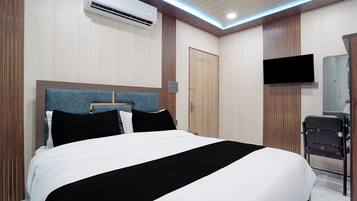 A hotel room with a bed, a flat-screen TV mounted on the wall, and an air conditioning unit above the bed.