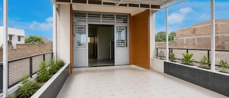 A balcony with a view of a brick building, a wooden door, and a tiled floor.