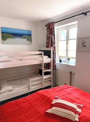 A bunk bed room with a red bedspread, a window with curtains, and a painting on the wall. - Achtern Diek 12c - Apartment 3 (Zingst)