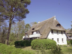 A traditional thatched-roof house with a white exterior, surrounded by greenery and trees. - Achtern Diek 12c - Apartment 3 (Zingst)