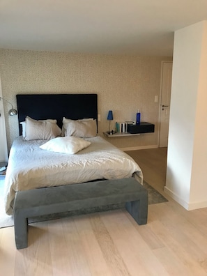 A bedroom with a bed, bedside table, lamp, and a door. - Exceptional duplex overlooking Saint-Malo in a private estate—with direct access to the beach (Dinard)
