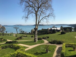 A park with a large tree, pathways, and a view of a body of water. - Exceptional duplex overlooking Saint-Malo in a private estate—with direct access to the beach (Dinard)
