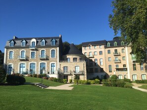 A large building with multiple balconies and a central tower, surrounded by well-maintained lawns and trees. - Exceptional duplex overlooking Saint-Malo in a private estate—with direct access to the beach (Dinard)