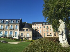 En historisk byggnad med flera våningar, ett torn och en staty i förgrunden.