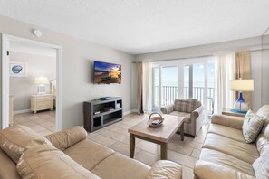 A living room with a sofa, a coffee table, a television, and a bookshelf. - Top Floor Beach Front - Beach Place #510 (Madeira Beach)