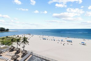 Ein Strand mit Liegestühlen und Sonnenschirmen, bewölkter Himmel und das Meer.