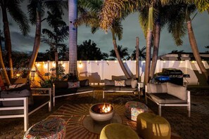 An outdoor seating area with sofas and a fire pit, surrounded by palm trees and string lights. - Tropical Oasis: Private Pool & BBQ (Lighthouse Point)