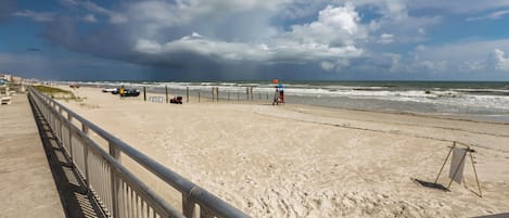 A beach with a metal railing, a lifeguard stand, and the ocean in the background.