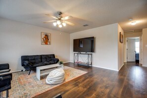 A living room with a black sofa, a white coffee table, a patterned rug, a ceiling fan, and a flat-screen TV mounted on the wall. - 7 Mi to Seaworld! Group-friendly Getaway w/ Pool (San Antonio)