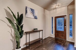 A hallway with a wooden floor, a potted plant, a console table with a small plant, a wall-mounted artwork, and a door with a window. - 7 Mi to Seaworld! Group-friendly Getaway w/ Pool (San Antonio)