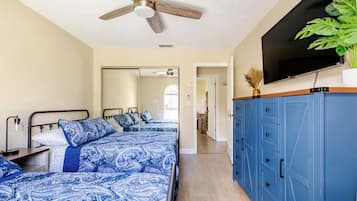 A bedroom with a bed, a ceiling fan, a TV, and a plant.