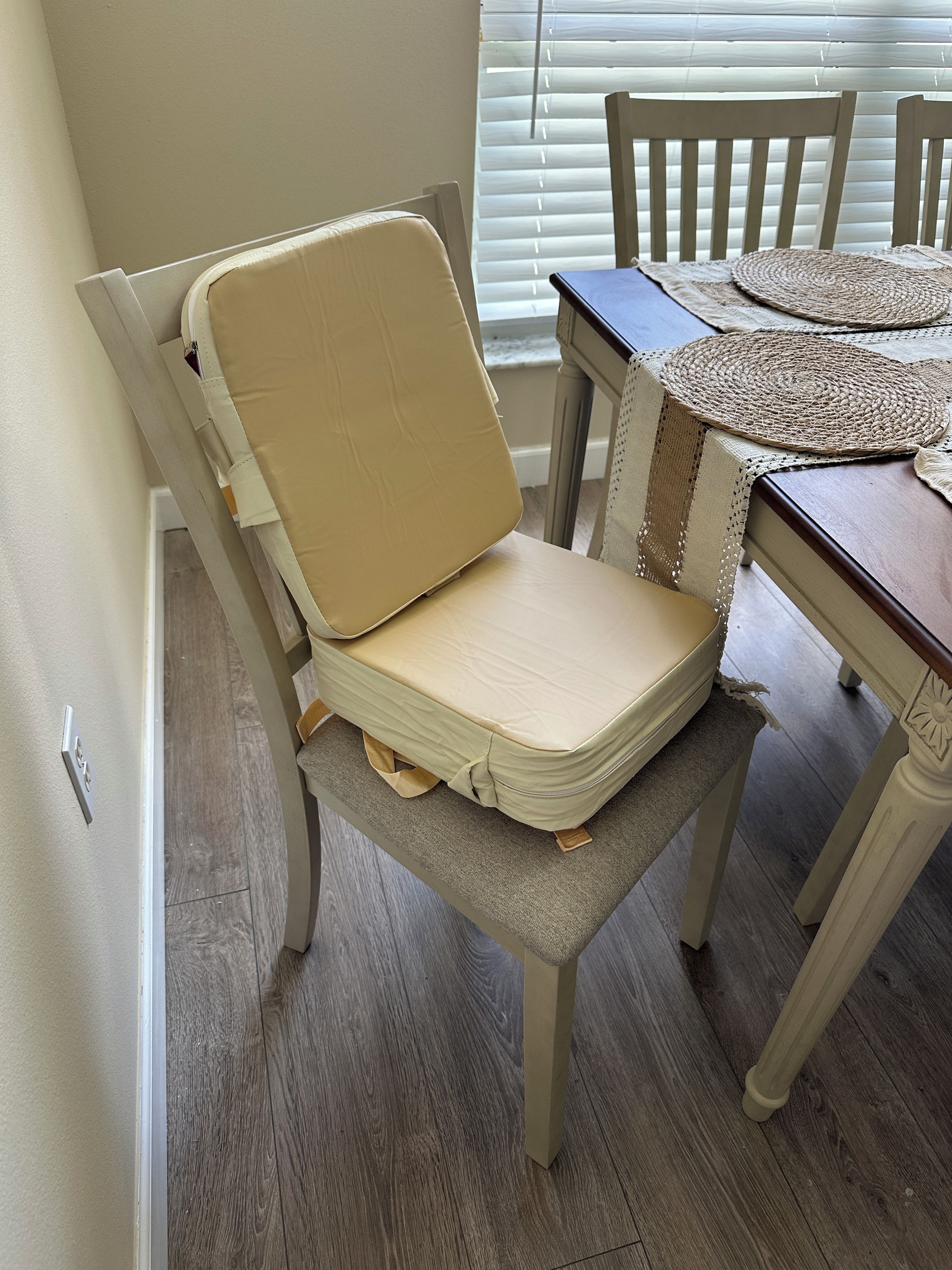 A dining area with a wooden table, a chair with a cushioned seat, and a window with blinds.