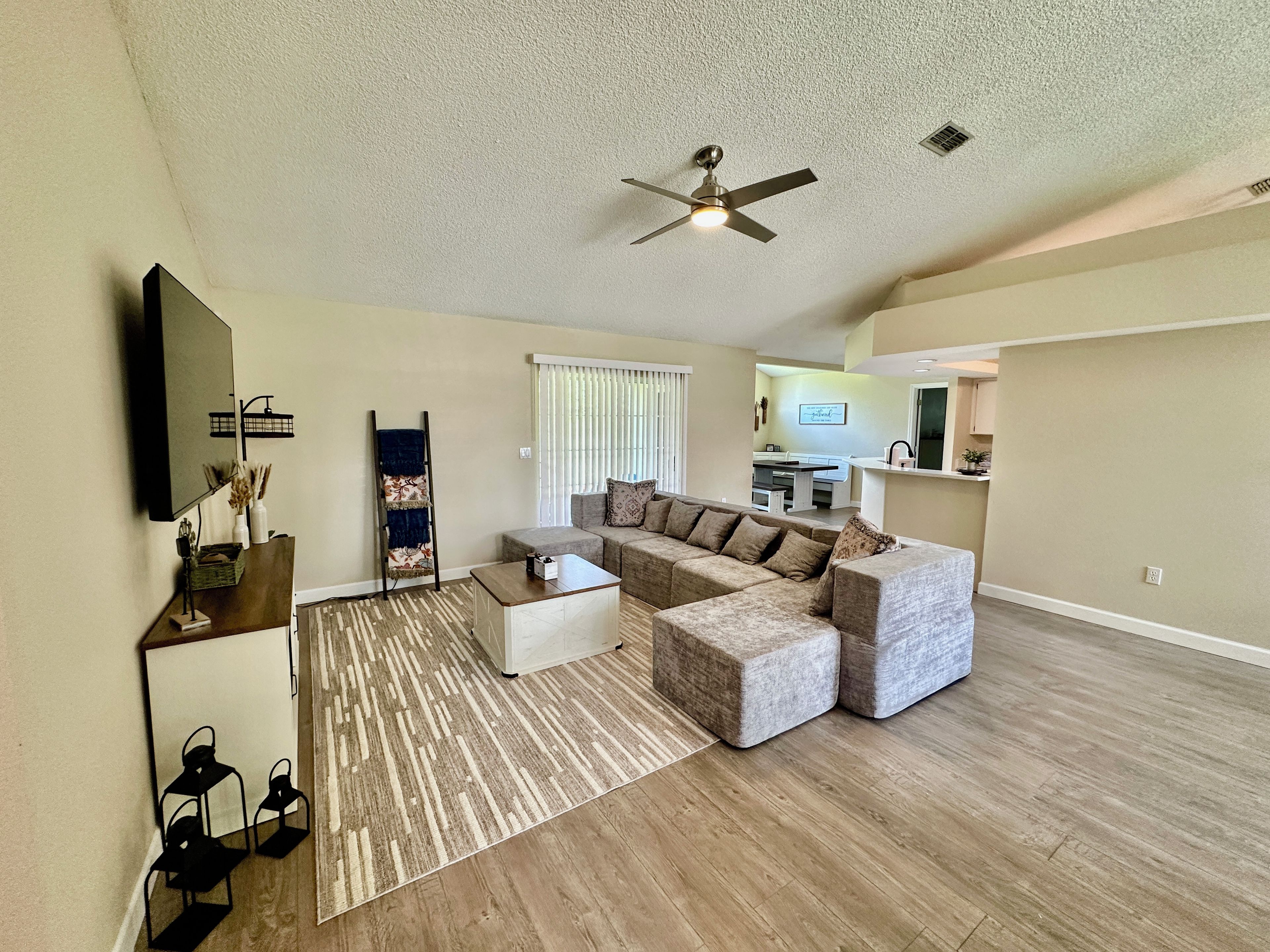 A spacious living room with a sectional sofa, a coffee table, a flat-screen TV, and a ceiling fan.