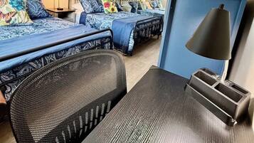 Ein Hotelzimmer mit zwei Betten, einem Deckenventilator, einem Schreibtisch mit Lampe und einer Zimmerpflanze.