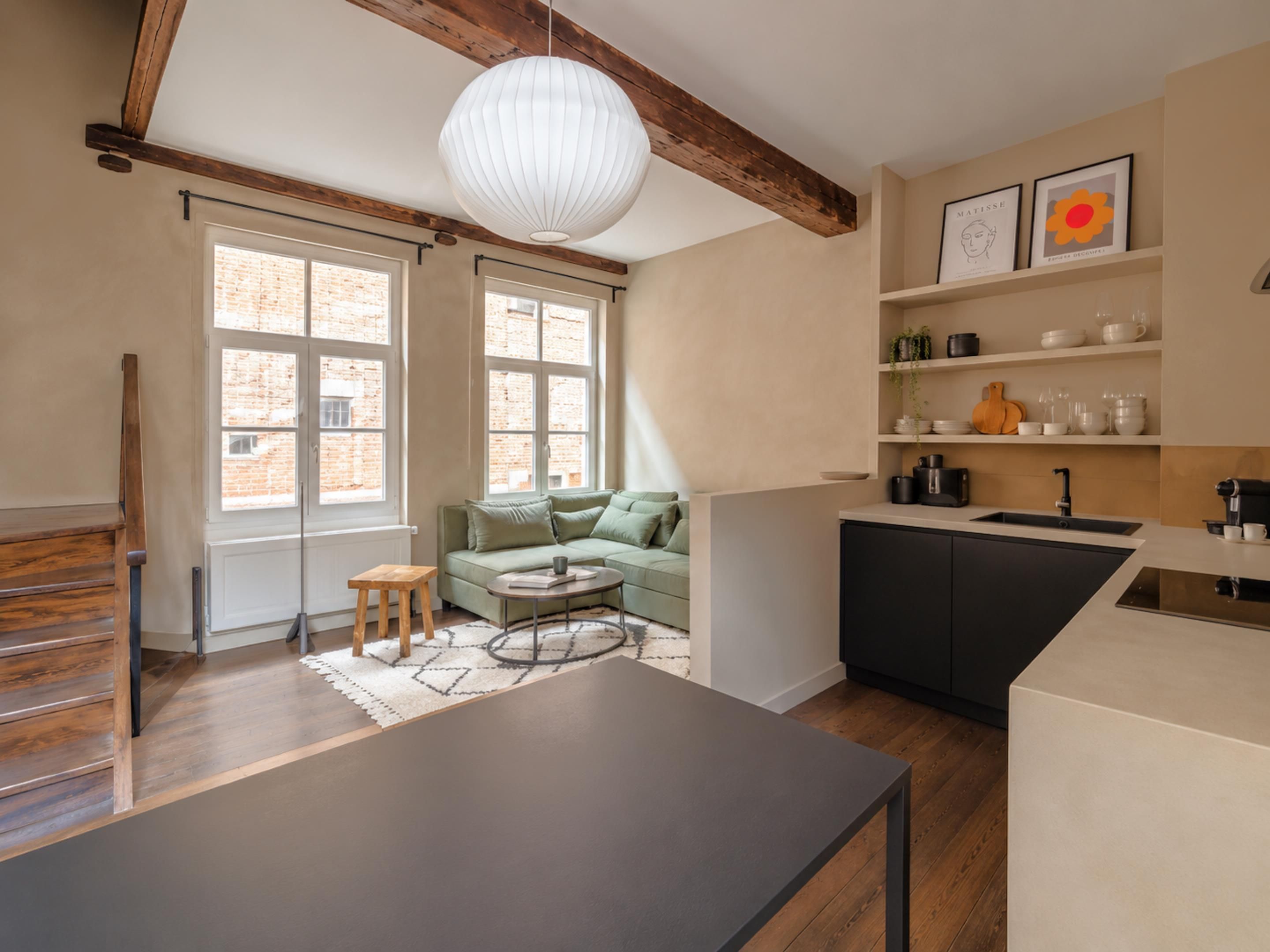 Een moderne keuken met een eethoek, grote ramen en een loft-stijl plafond.