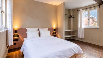 Ein Schlafzimmer mit Holzboden, einem Bett mit weißer Bettwäsche und einem Fenster mit Blick auf Gebäude.