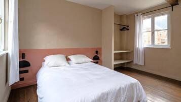 A bedroom with a bed, a window, a coat rack, and a wooden floor.