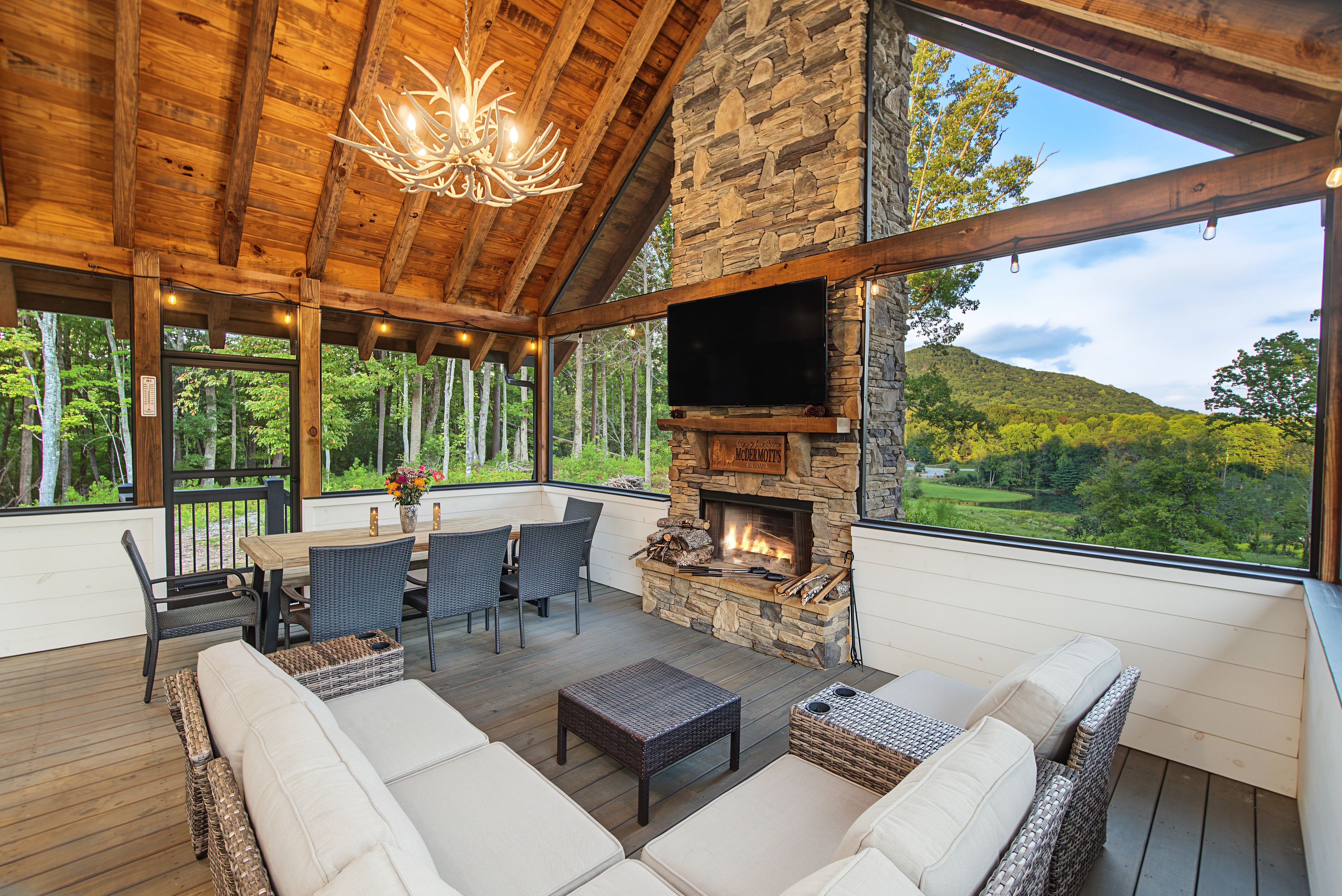 A wooden deck with outdoor seating, a stone fireplace, and a TV mounted on the wall.