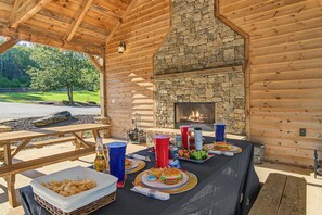 An outdoor dining area with a stone fireplace, picnic tables, and a view of the surrounding landscape. - A Long Way From Durrow (Sautee Nacoochee)
