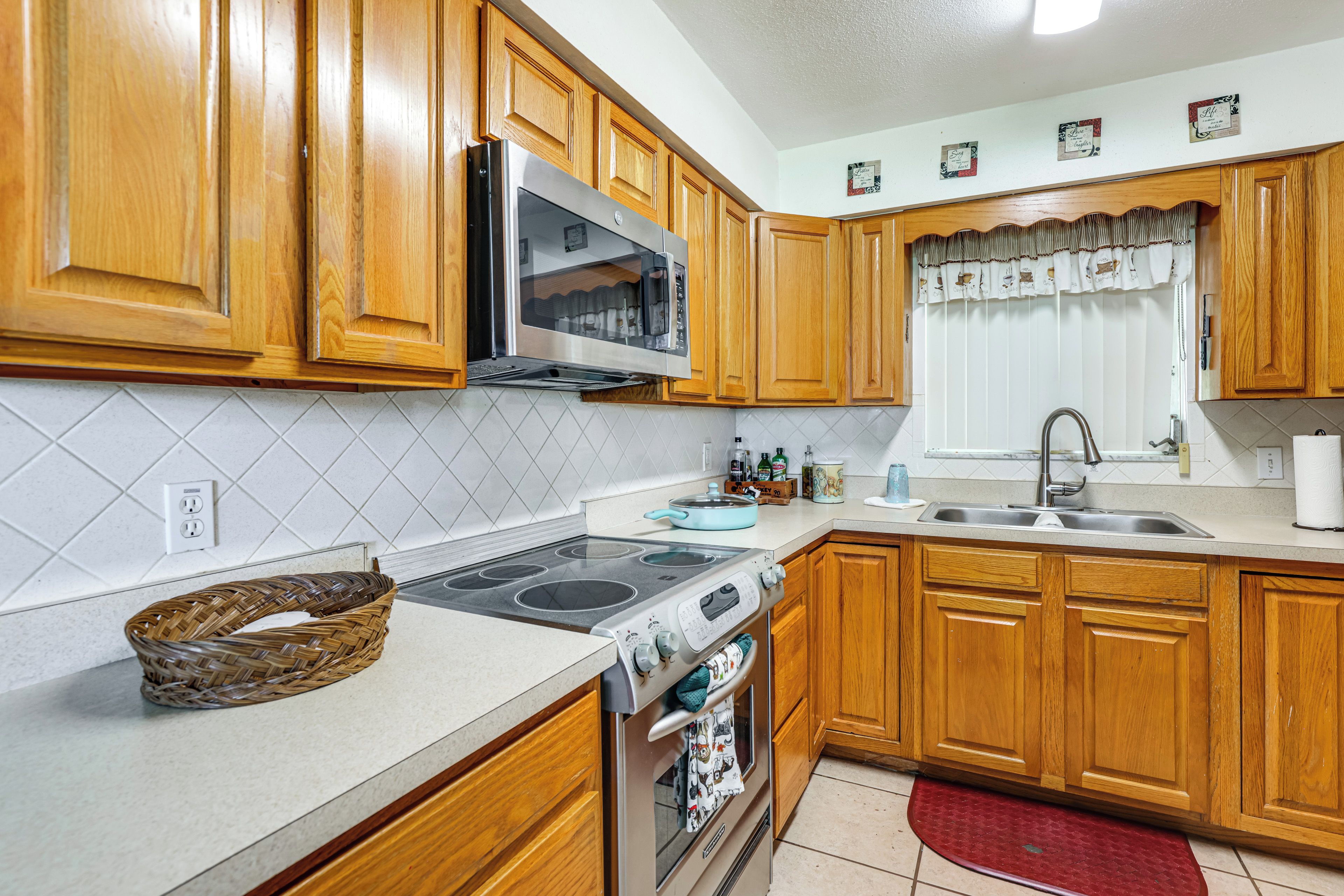 A kitchen with wooden cabinets, a stainless steel range, a microwave, and a double sink.