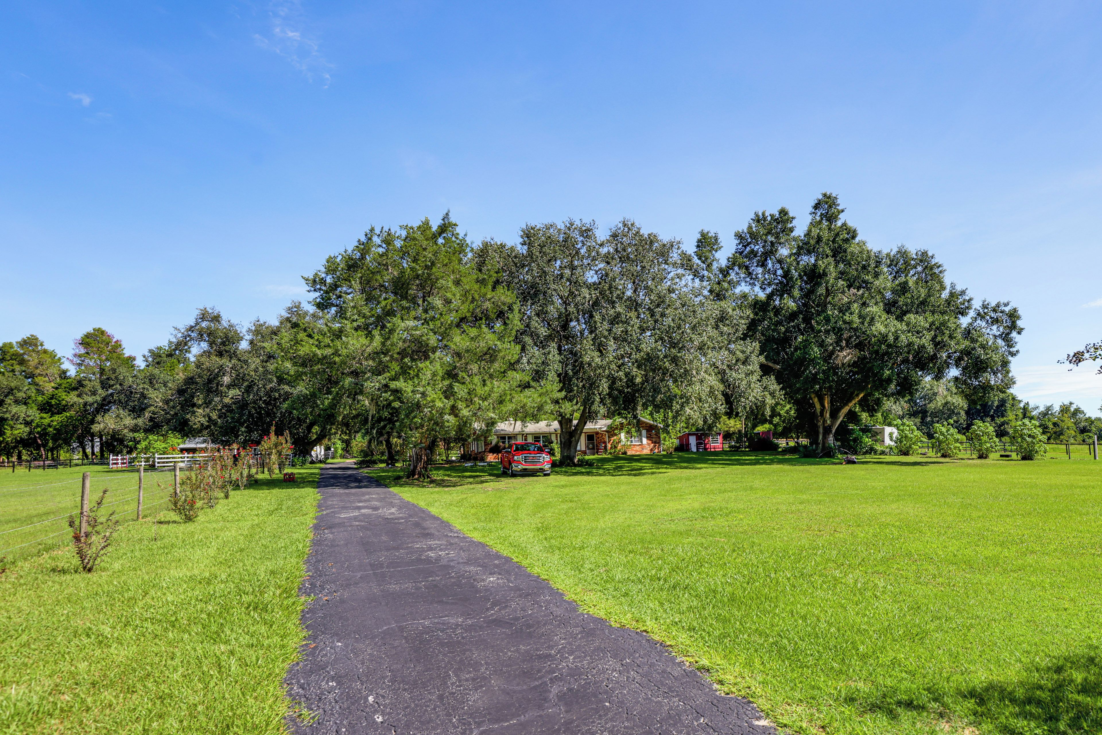 A pathway leading to a rural property with a house and a red truck.