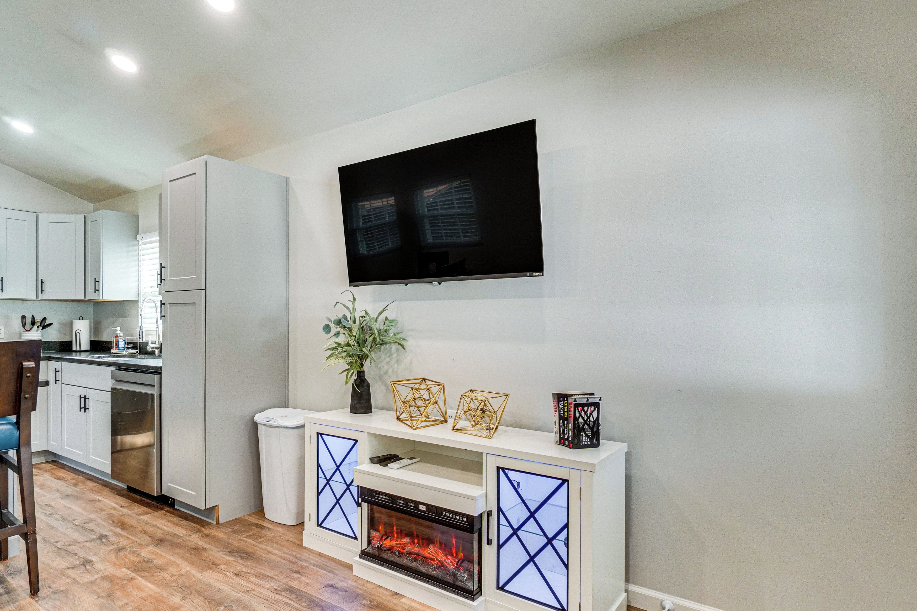 A modern kitchen with white cabinets, a built-in oven, and a fireplace with a glass door.