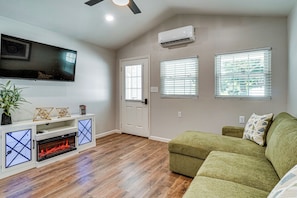 A living room with a flat-screen TV, a fireplace, a green sofa, and a ceiling fan. - New To Market Riverfront Pigeon Forge Retreat (Pigeon Forge)
