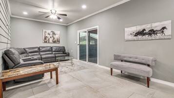 A living room with a gray leather sofa, a gray armchair, a glass coffee table, and two wall-mounted horse paintings.