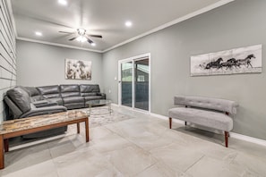 A living room with a gray leather sofa, a gray armchair, a glass coffee table, and two wall-mounted horse paintings. - San Benito Home w/ Pool, Close to Dtwn (San Benito)