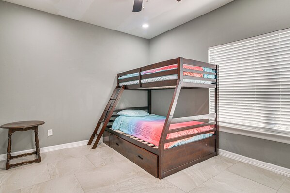 A bunk bed with a ladder, a small table, and a window with blinds.