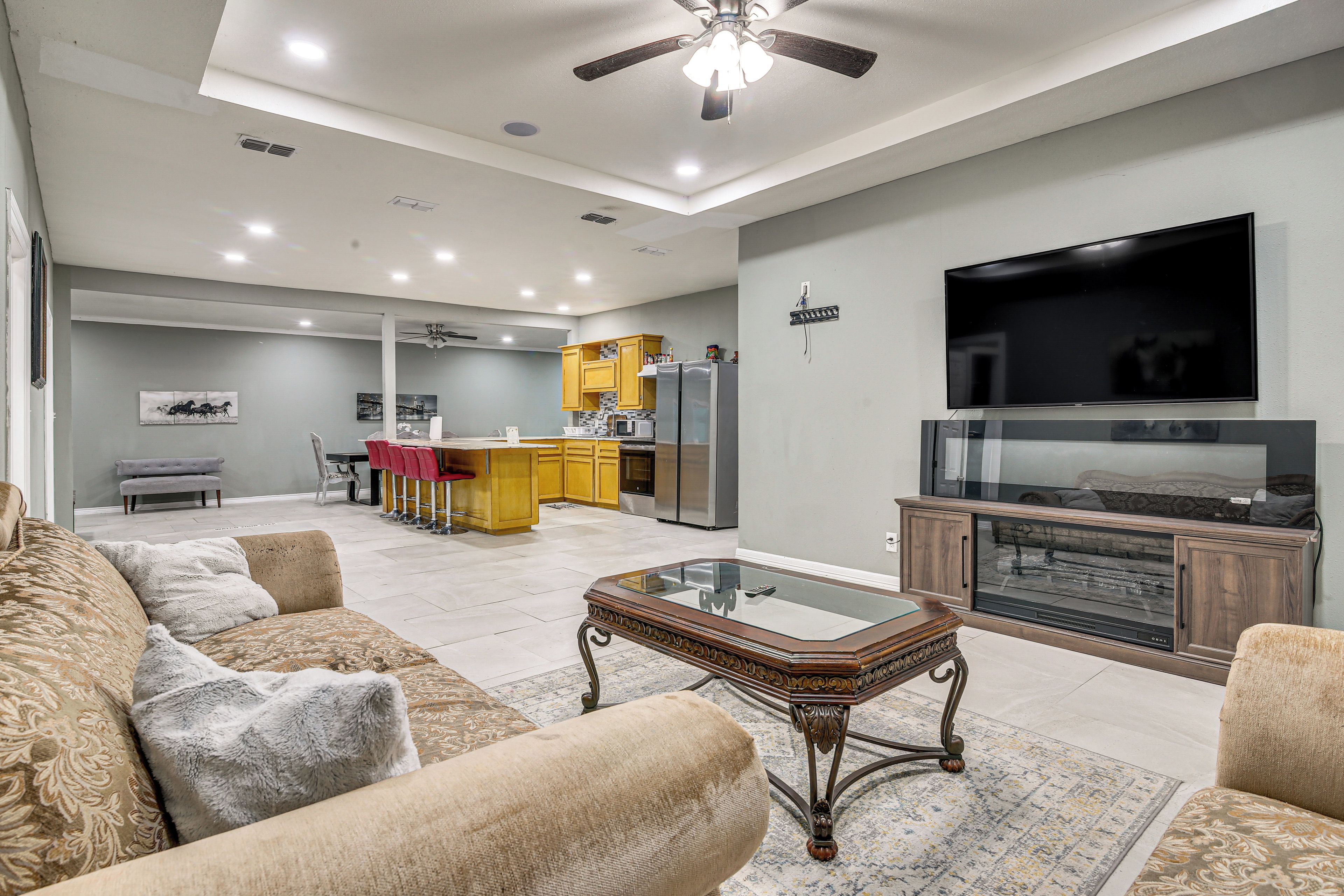 A spacious living room with a sofa, a glass coffee table, and a flat-screen TV mounted on the wall.
