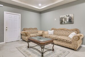 A living room with a beige patterned sofa, a glass-top coffee table, and a painting of horses on the wall.