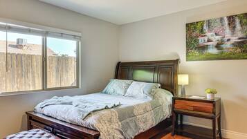 A bedroom with a bed, a wooden bench, a nightstand with a lamp, and a painting of a waterfall.