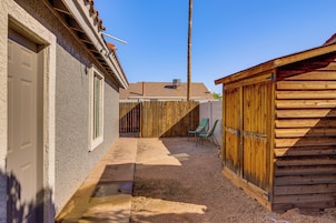 A narrow driveway leading to a garage with a wooden fence and a green chair.