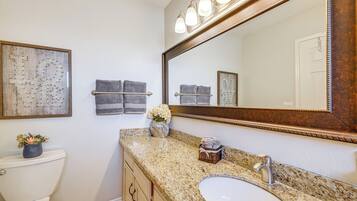 A bathroom with a toilet, sink, vanity, mirror, towel rack, and decorative wall art.
