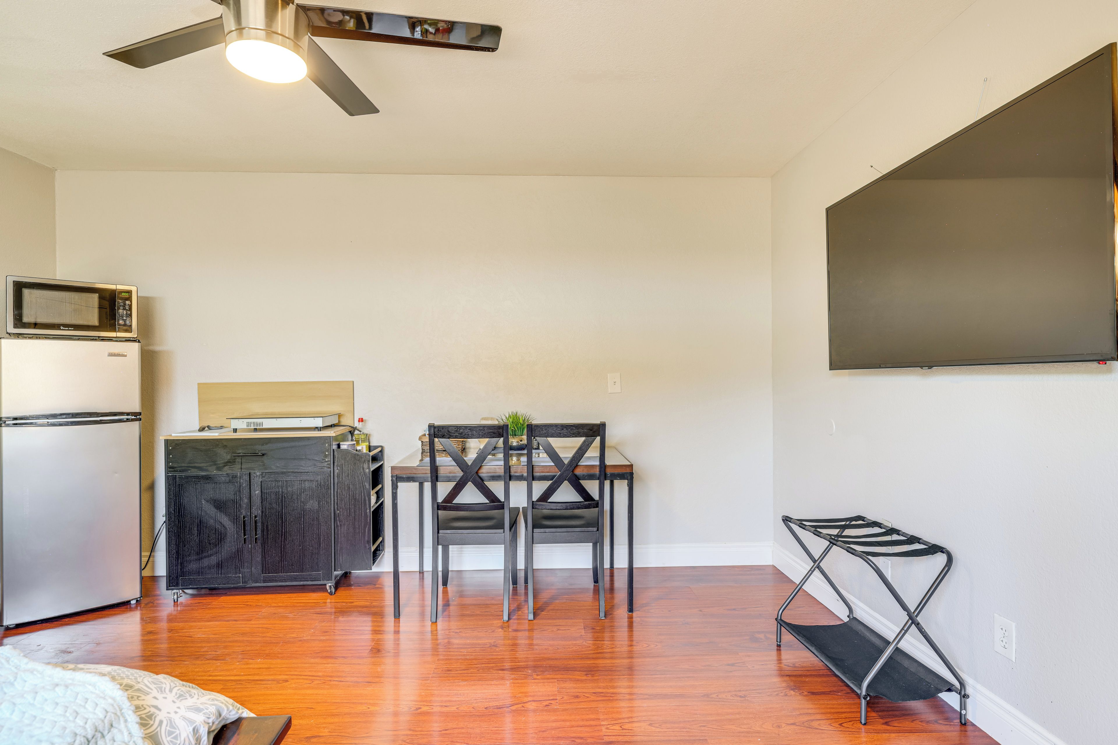 Un espacio habitable compacto con kitchenette, una zona de comedor con dos sillas, ventilador de techo y televisor de pantalla plana montado en la pared.