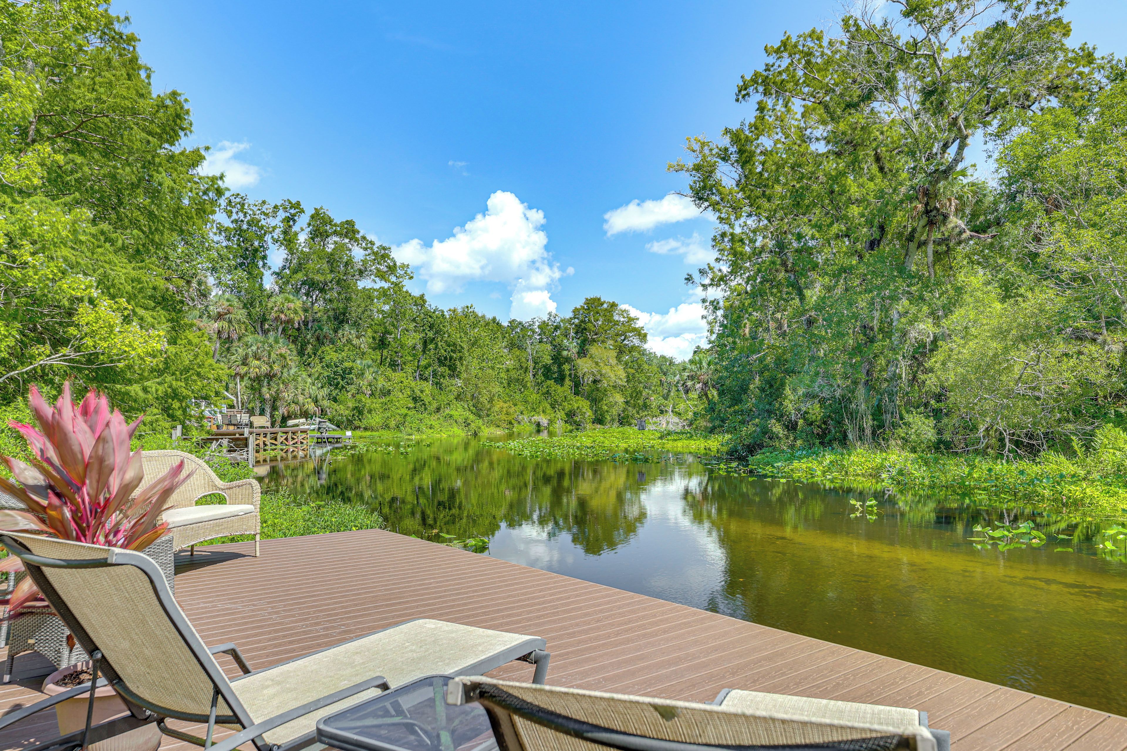 A wooden deck with lounge chairs overlooking a calm pond surrounded by lush greenery.
