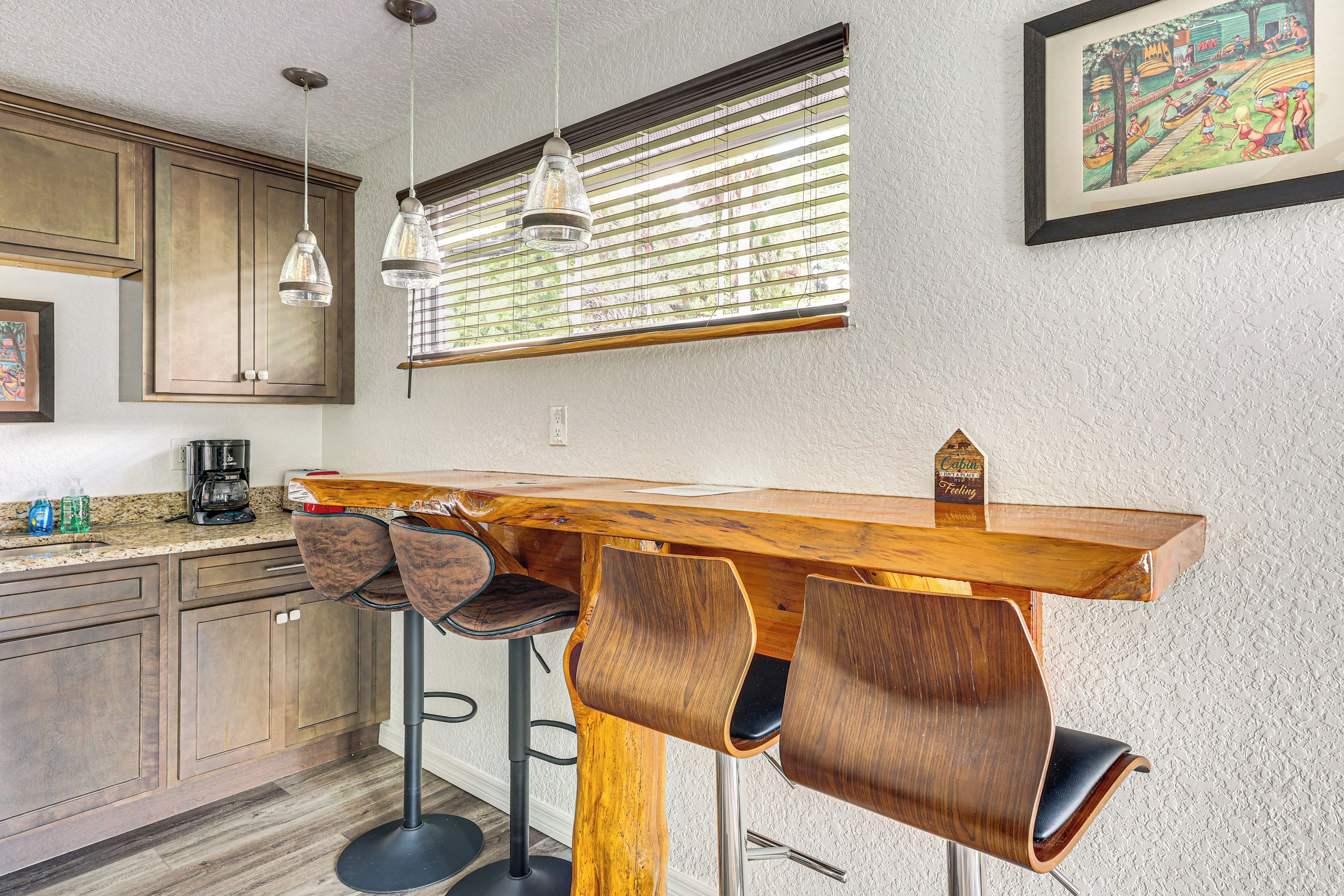 A kitchen with a wooden bar counter, stools, pendant lights, and a window with blinds.