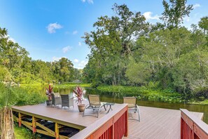 A wooden deck with outdoor furniture overlooking a calm river, surrounded by lush greenery and trees. - Waterfront Studio Cabin on Rock Springs Run! (Apopka)